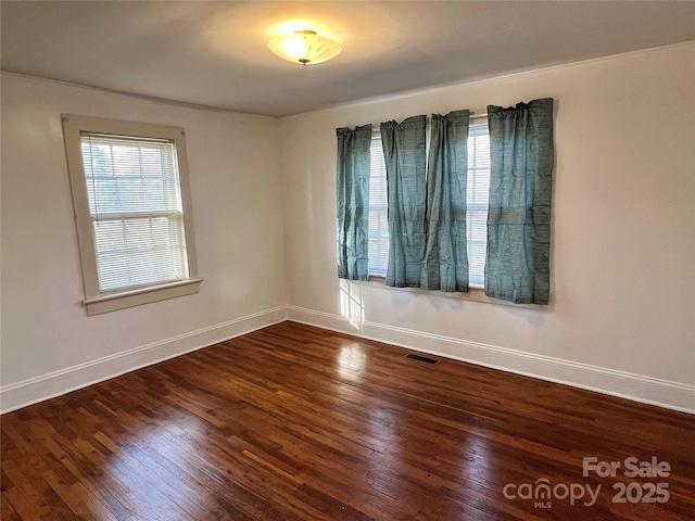 unfurnished room with visible vents, wood finished floors, and baseboards