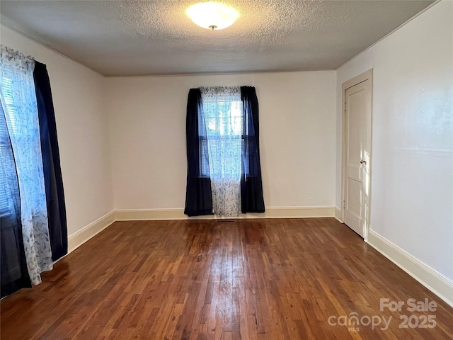 unfurnished room with dark wood finished floors, a textured ceiling, and baseboards