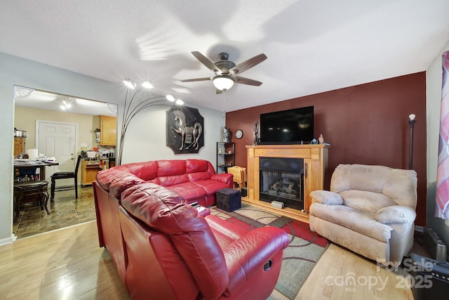 living room with a textured ceiling, a fireplace with raised hearth, light wood-style floors, and ceiling fan