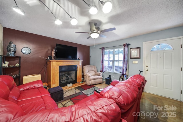 living area with a glass covered fireplace, a textured ceiling, wood finished floors, and a ceiling fan