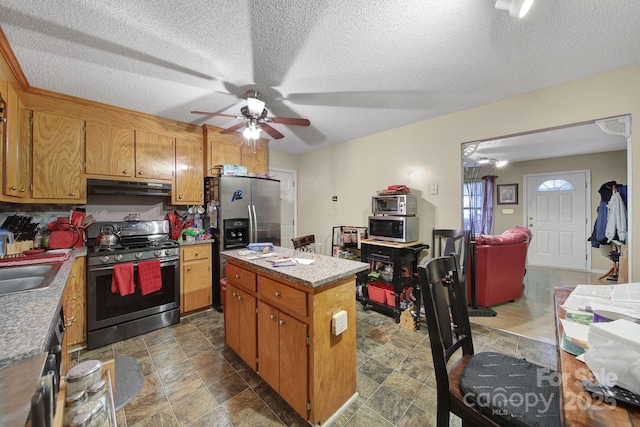 kitchen with ceiling fan, stone finish floor, under cabinet range hood, appliances with stainless steel finishes, and a center island