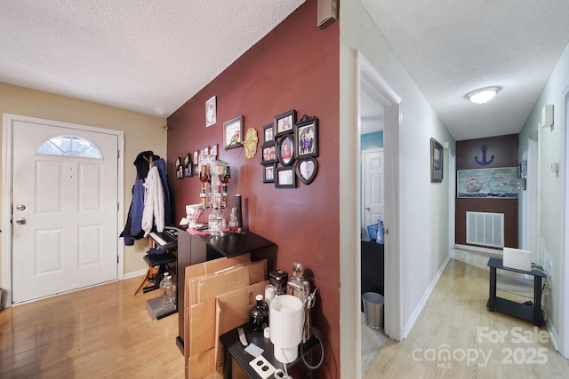 entryway featuring visible vents, a textured ceiling, baseboards, and wood finished floors