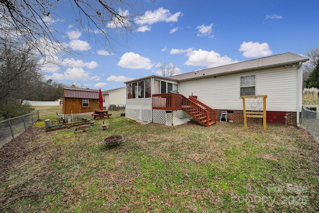 rear view of property featuring an outdoor structure, a fire pit, fence, and a sunroom