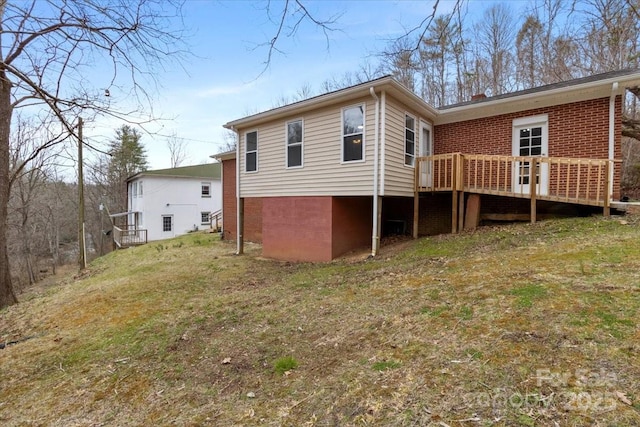 back of property with a wooden deck, brick siding, and a lawn