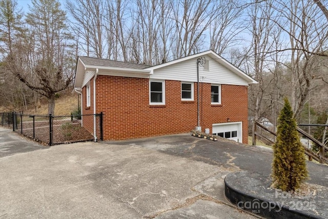 view of side of home with aphalt driveway, an attached garage, fence, and brick siding