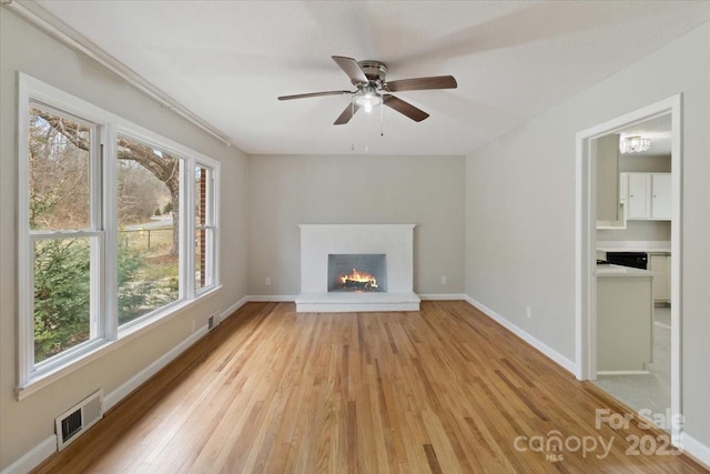 unfurnished living room with visible vents, a brick fireplace, baseboards, light wood-style floors, and a ceiling fan