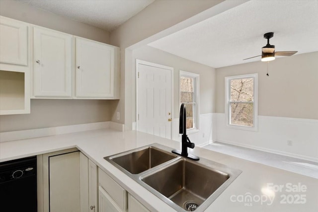 kitchen with a sink, black dishwasher, white cabinets, and light countertops