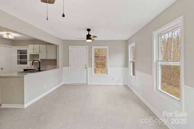 interior space with baseboards, ceiling fan, light countertops, a peninsula, and a sink