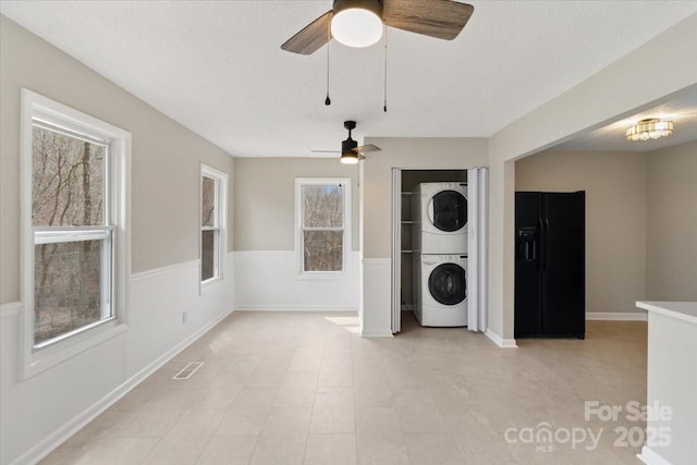 laundry area with a wainscoted wall, laundry area, stacked washer and clothes dryer, and a textured ceiling