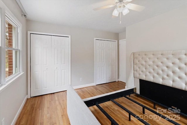 bedroom with ceiling fan, wood finished floors, multiple closets, and baseboards