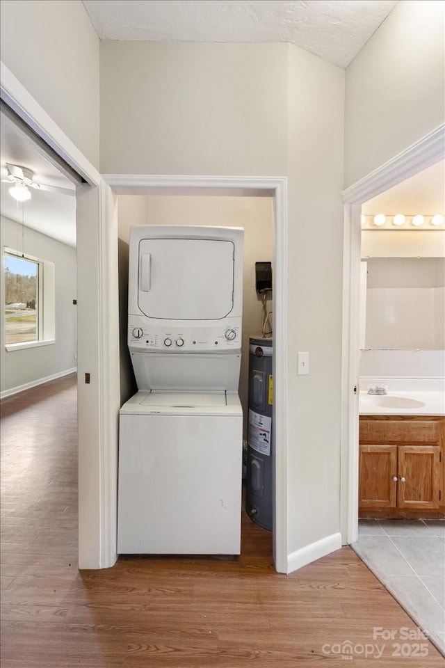 laundry area with electric water heater, light wood-type flooring, stacked washer and dryer, laundry area, and a sink