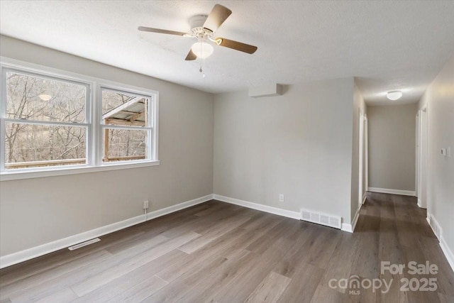 unfurnished room with visible vents, baseboards, wood finished floors, and a ceiling fan