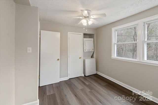 unfurnished bedroom featuring a textured ceiling, stacked washer / drying machine, baseboards, ceiling fan, and dark wood-style flooring