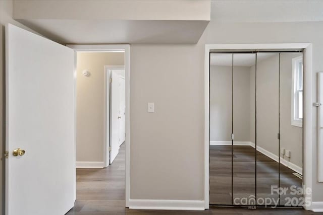 unfurnished bedroom featuring wood finished floors, baseboards, and a closet