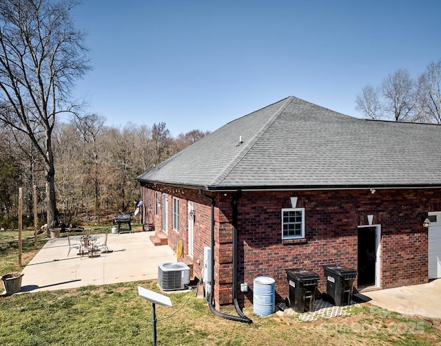 view of home's exterior with a lawn, a patio, central AC, roof with shingles, and brick siding