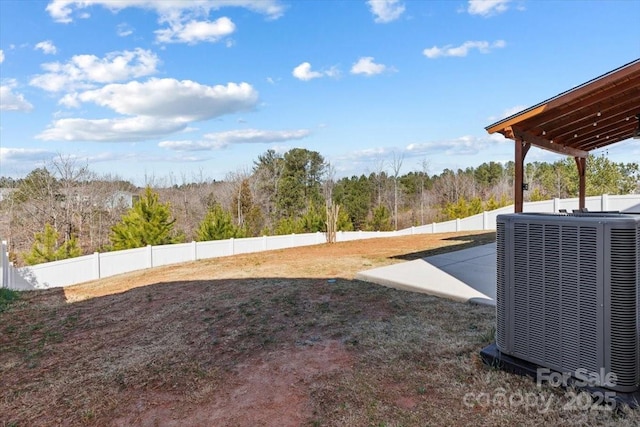 view of yard featuring central air condition unit, a view of trees, and fence