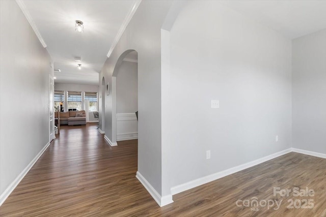 hallway with baseboards, arched walkways, wood finished floors, and ornamental molding