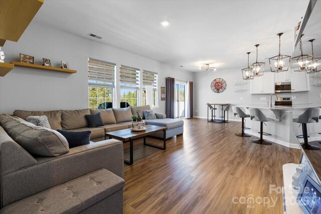 living area with visible vents, baseboards, an inviting chandelier, and dark wood-style flooring