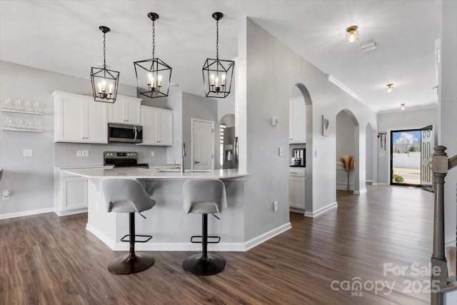 kitchen featuring a breakfast bar, decorative backsplash, arched walkways, stainless steel appliances, and dark wood-style flooring