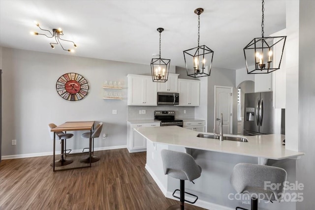 kitchen featuring a peninsula, a sink, decorative backsplash, appliances with stainless steel finishes, and a kitchen breakfast bar