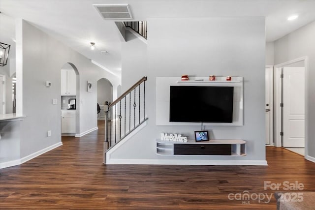 unfurnished living room with stairway, wood finished floors, visible vents, baseboards, and arched walkways