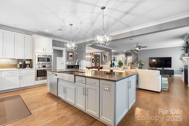 kitchen featuring light wood finished floors, a center island with sink, ornamental molding, appliances with stainless steel finishes, and a sink