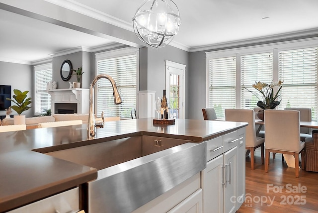 kitchen with pendant lighting, ornamental molding, wood finished floors, a fireplace, and a chandelier