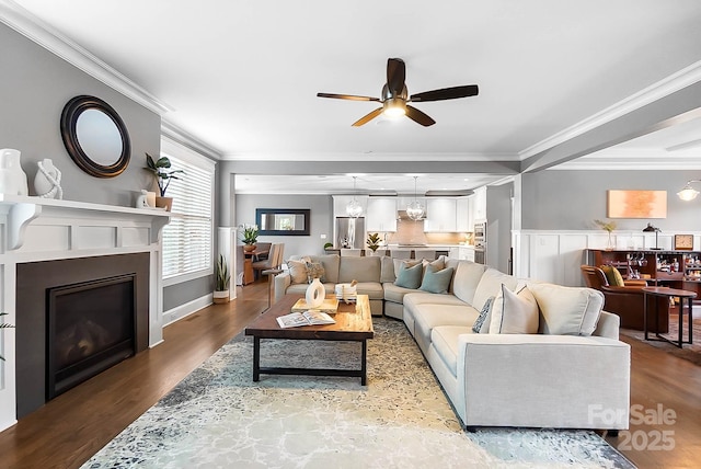 living room with a fireplace, wood finished floors, a ceiling fan, and ornamental molding