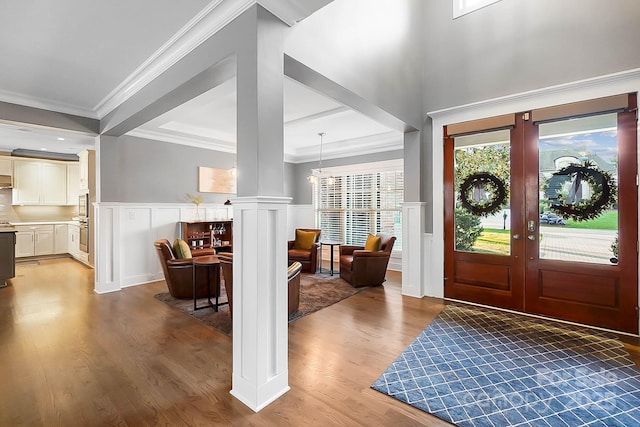 entrance foyer with decorative columns, wood finished floors, a wainscoted wall, and ornamental molding