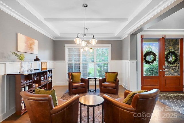 sitting room with a raised ceiling, a notable chandelier, wood finished floors, and wainscoting