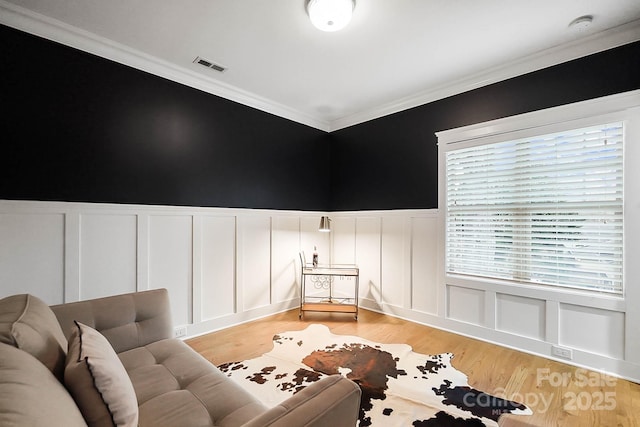 sitting room featuring crown molding, light wood-style flooring, visible vents, and wainscoting