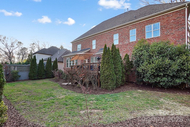 rear view of house featuring a lawn, a deck, brick siding, and fence