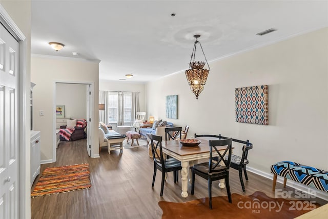 dining room with visible vents, wood finished floors, baseboards, and ornamental molding