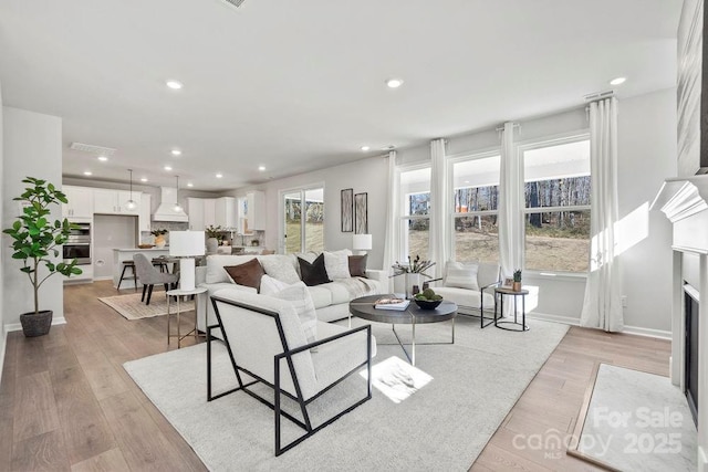 living area featuring a fireplace with flush hearth, recessed lighting, light wood-type flooring, and baseboards