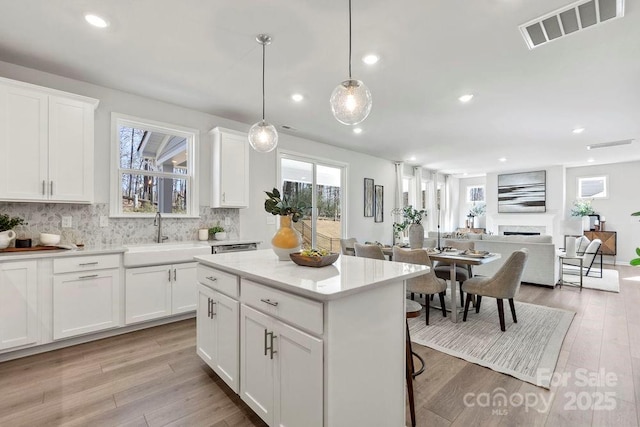 kitchen with visible vents, open floor plan, light wood-type flooring, a fireplace, and a sink