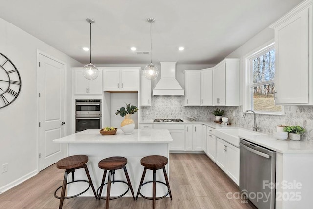 kitchen with a sink, custom range hood, white cabinetry, and stainless steel appliances