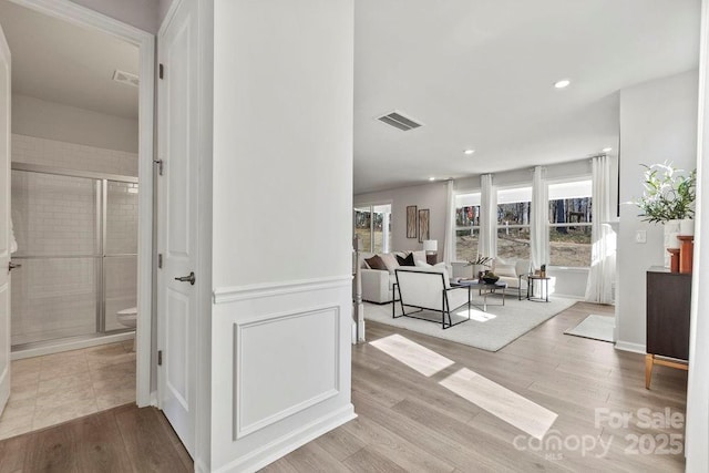 hall featuring visible vents, recessed lighting, a decorative wall, and wood finished floors