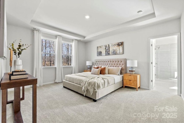 bedroom with ensuite bath, a raised ceiling, baseboards, and light carpet