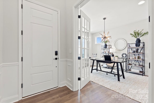 foyer entrance featuring a notable chandelier, wood finished floors, and wainscoting