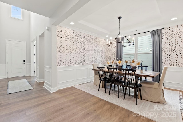 dining space with a tray ceiling, wainscoting, an inviting chandelier, wood finished floors, and a decorative wall