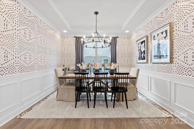 dining room featuring wallpapered walls, a tray ceiling, a decorative wall, and wood finished floors