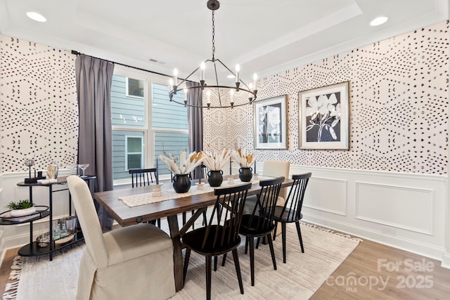 dining space featuring light wood-type flooring, a raised ceiling, a wainscoted wall, and a decorative wall