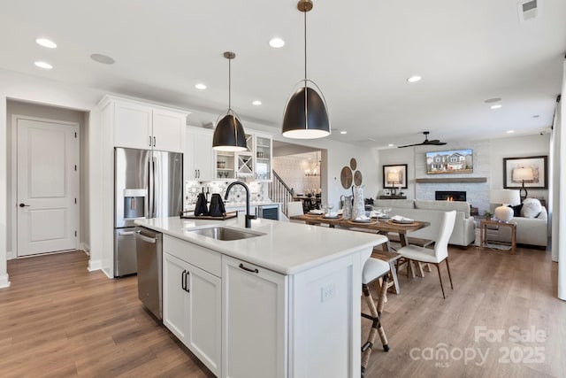 kitchen with visible vents, an island with sink, a sink, stainless steel appliances, and a large fireplace