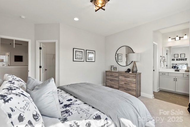 bedroom with recessed lighting, light colored carpet, ensuite bath, and baseboards