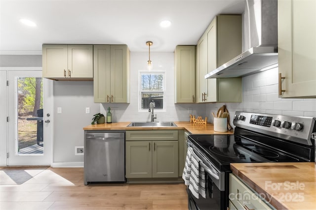 kitchen with green cabinets, wall chimney range hood, butcher block counters, stainless steel appliances, and a sink