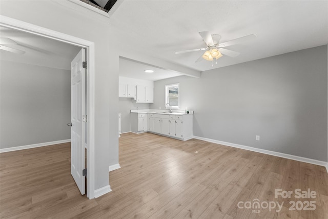 unfurnished living room featuring light wood-style flooring, a ceiling fan, baseboards, and a sink