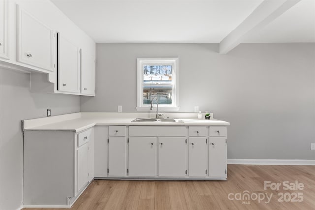 kitchen with baseboards, light countertops, light wood-type flooring, white cabinets, and a sink