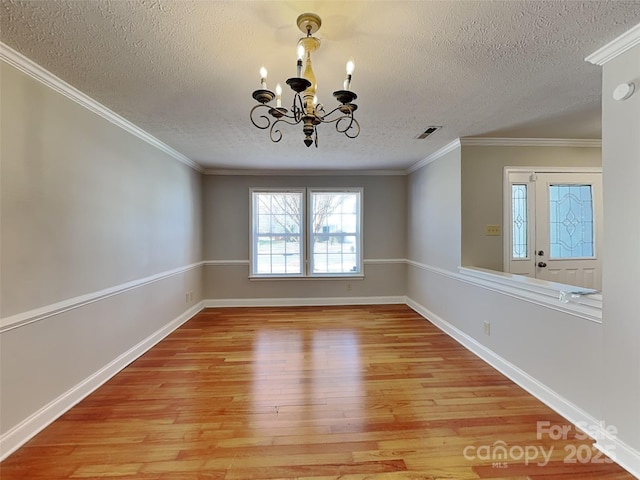 empty room with visible vents, crown molding, baseboards, light wood-type flooring, and a notable chandelier