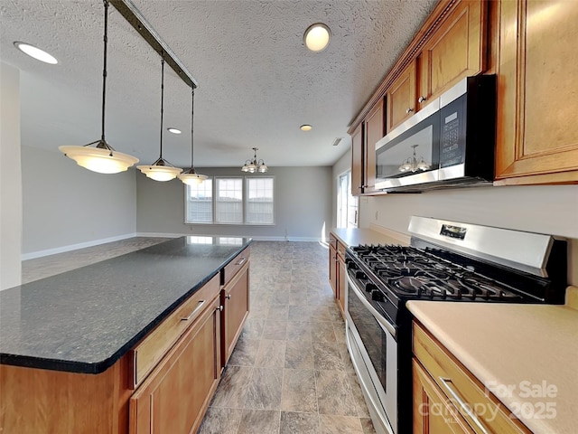 kitchen featuring dark countertops, baseboards, decorative light fixtures, brown cabinetry, and stainless steel appliances