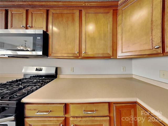 kitchen featuring stainless steel appliances, brown cabinetry, and light countertops